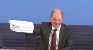 Olaf Scholz zeigt bei der Pressekonferenz einen Stapel mit den beschlossenen Gesetzen