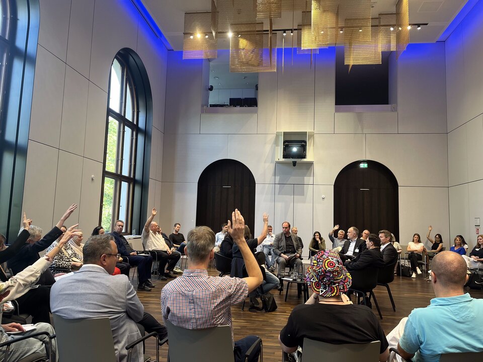 Die Expert/innen diskutieren beim Fishbowl-Format nicht auf einer erhöhten Bühne sondern mitten unter den Zuschauer/innen, die wie hier nach ihrer Meinung gefragt werden oder sich aktiv "dazusetzen" und mitdiskutieren können.